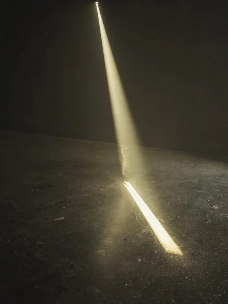 A single hard shaft of warm morning light crossing a dark concrete floor, fine dust suspended in the beam.